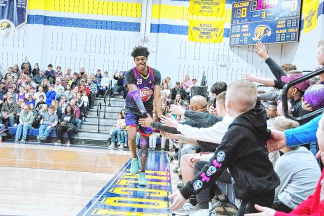 A Harlem Wizards basketball player trots around the perimeter of the court while greeting the fans.